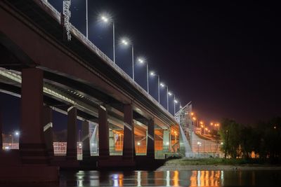 Illuminated bridge over river against sky at night