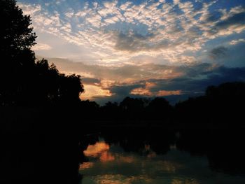 Silhouette trees by lake against sky during sunset