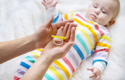 Mother holding pacifier while baby lying on bed