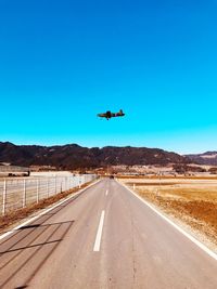 Airplane flying over road against clear blue sky