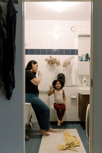 Mother and daughter brushing teeth together in bathroom at home