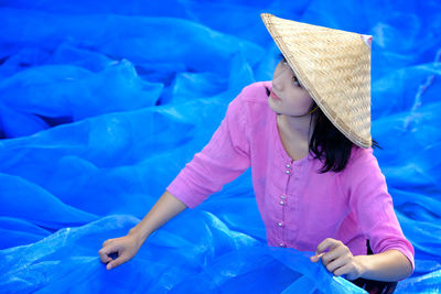 Young woman wearing asian style conical hat holding blue tulle netting