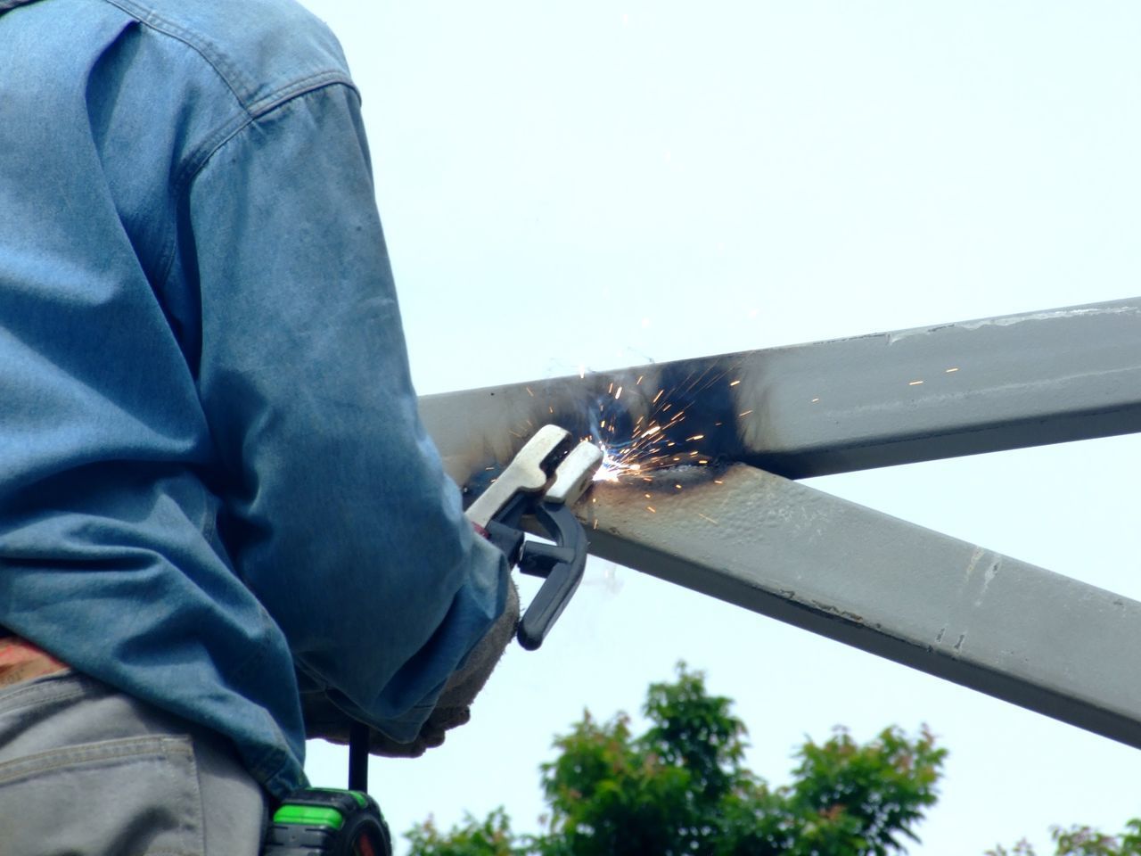 LOW ANGLE VIEW OF MAN WORKING ON METAL AGAINST SKY