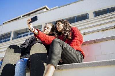 Low angle view of girls taking selfie while sitting outdoors