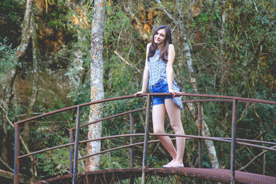 Portrait of young woman standing by railing in forest