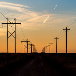 Electricity pylons by road against sky during sunset