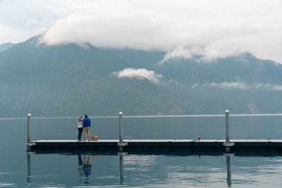 Man and woman standing on dock looking at foggy mountans