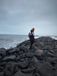 Man standing on rock at beach against sky