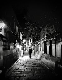 Rear view of man walking on footpath amidst buildings at night