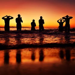 Silhouette people on shore against orange sky