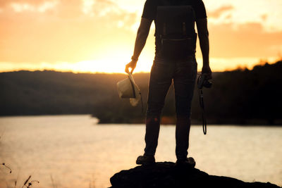 Low section of man standing on rock against sea during sunset