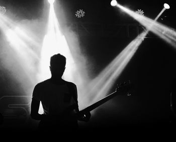 Silhouette man  standing playing guitar in illuminated music concert