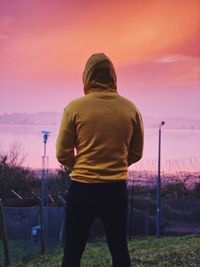Rear view of man standing on field against sky during sunset