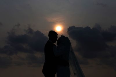 Silhouette wedding couple against sky during sunset