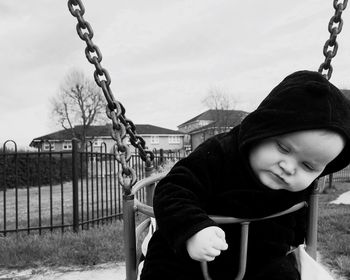 Close-up of baby boy sitting on swing against sky