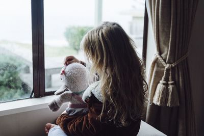 Girl playing with toy while sitting by window at home