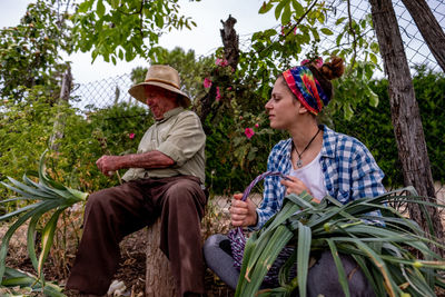 Side view of two women sitting against plants