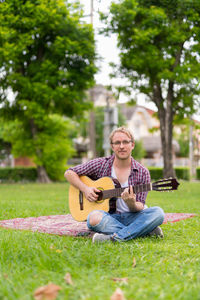 Portrait of man playing guitar while sitting at park