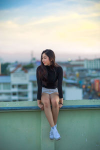 Young woman sitting on railing against cityscape