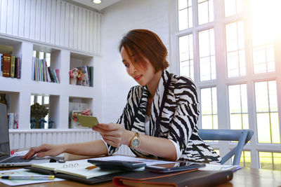 Young woman using phone while sitting on table