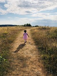 Rear view of girl walking on field against sky