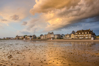 Buildings by sea against sky during sunset