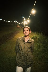 Portrait of young woman at night standing on hill with lights