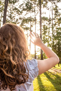 Rear view of girl with long hair shielding eyes at forest