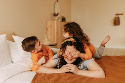 A happy mother hugs children a little boy and a girl sitting on a bed in a cozy interior of  house