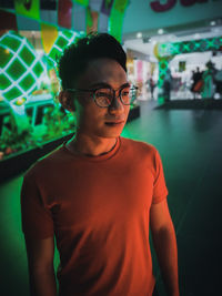 Young man wearing eyeglasses standing against store at night