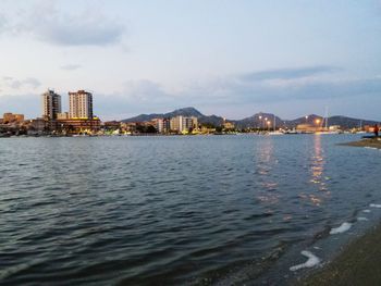 View of city at waterfront against cloudy sky