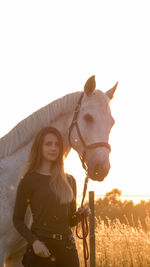 Portrait of young woman standing with horse on field against sky