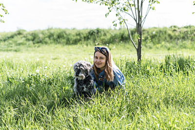 Young blond woman resting with fluffy dog on green grass in summer, pet love and care, walking 