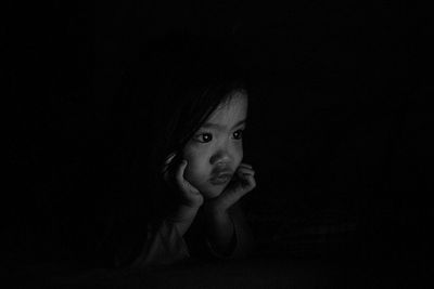 Close-up of girl sitting against black background