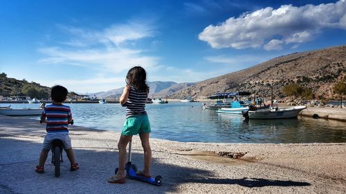 Rear view of girl with push scooter by boy against lake