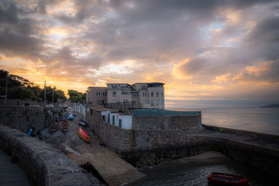 Buildings by sea against sky during sunset