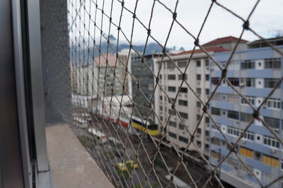 Close-up of city seen through chainlink fence