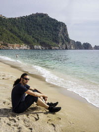 Woman sitting on beach by sea against sky