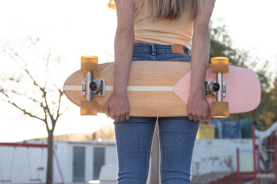 Impersonal close up portrait of a slim young girl holding natural vintage skateboard behind her back