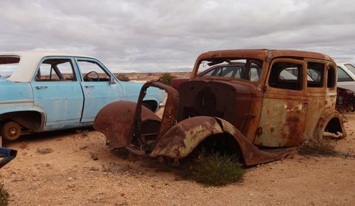 Abandoned car on land against sky