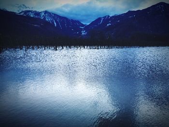 Scenic view of lake by snowcapped mountains against sky