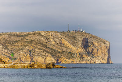 Lighthouse on rock by sea against sky