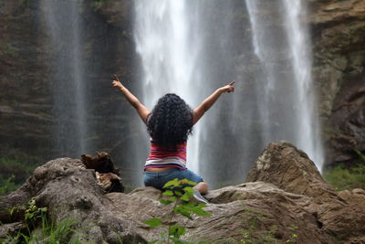 Rear view of woman standing on rock against waterfall