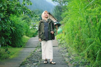 Portrait of woman standing on footpath amidst plants