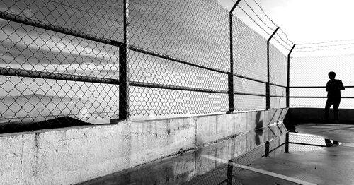 Rear view of silhouette mid adult man standing by fence against sky