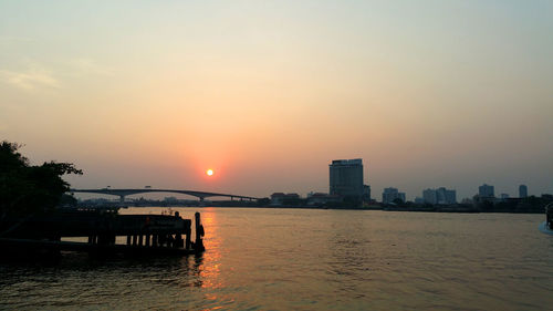 Buildings by sea against sky during sunset