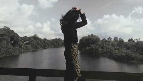 Woman standing on bridge over lake against sky