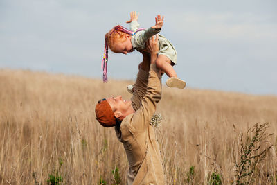 Father plays with his little daughter in field. holding high in arms, baby flying. family  outdoors