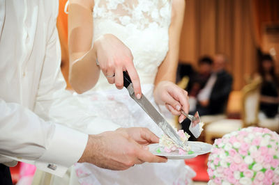 Midsection of bride holding knife with cake on plate by waiter