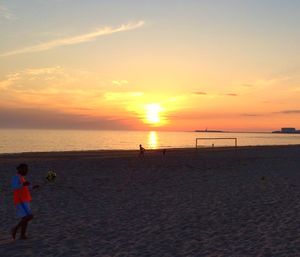 Boy standing on beach against sky during sunset